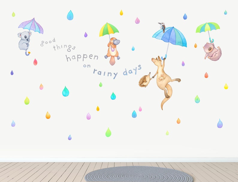 May include: Wall decal featuring a colorful quote, "Good things happen on rainy days", with various animals holding umbrellas, including a koala, a platypus, a kangaroo, and a wombat. The background is white with colorful raindrops.