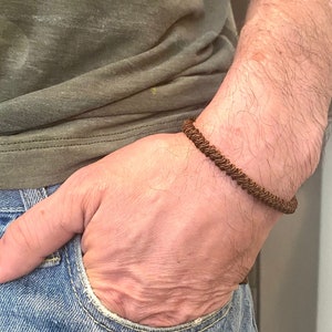 Puede incluir: Un brazalete de cuero trenzado marrón en la muñeca de una persona.