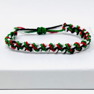 Puede incluir: Un brazalete de amistad trenzado con hilo rojo, blanco, verde y negro.