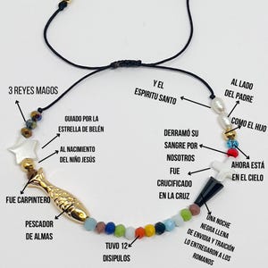 May include: A colorful beaded bracelet with a gold fish charm, a white star charm, and a white cross charm. The bracelet has text in Spanish describing the significance of each charm.