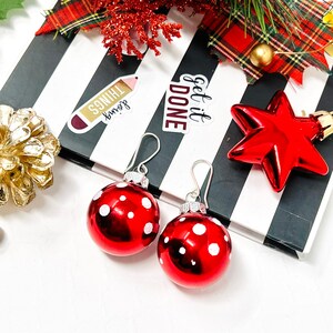 May include: A pair of red and white polka dot earrings with silver hooks. The earrings are on a black and white striped surface with the words "Get it Done" and "Second Things" written on stickers.