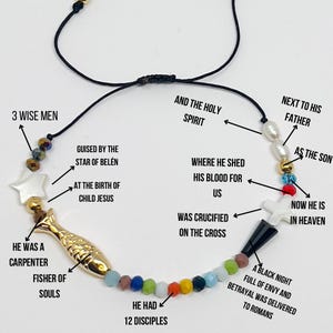 May include: A black string necklace with colorful beads and charms, including a gold fish, a white star, and a white cross. The necklace represents the life of Jesus Christ, with text describing his journey from birth to death and resurrection.