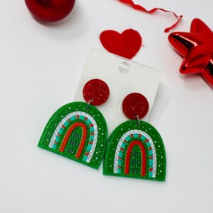 May include: Green and red glitter Christmas earrings with a rainbow design and the words "Ho Ho Ho" on each earring.
