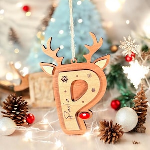 May include: Wooden Christmas ornament shaped like a reindeer head with the letter "P" cut out. The ornament is decorated with snowflakes and the name "Paola" is engraved on the side.