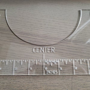 May include: A clear plastic measuring tool with a curved shape for measuring chest size. The tool has a ruler marked in inches and the words "RIGHT CHEST GUIDE", "LEFT CHEST GUIDE", and "CENTER" printed on it.