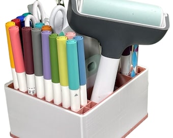 Puede incluir: Organizador impreso en 3D blanco y rosa con compartimentos para bolígrafos, marcadores y herramientas. El organizador tiene una herramienta de rodillo y una variedad de marcadores de colores.