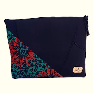 Könnte beinhalten: Eine marineblaue Clutch mit einem dekorativen Blumenmuster in Rot und Grün. Die Clutch hat ein einzigartiges Design mit einem Holzschild mit der Aufschrift "nalu". Die Tasche hat einen Kordelzugverschluss.