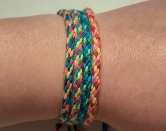 May include: Braided friendship bracelets in a variety of colors, including blue, pink, yellow, and red. The bracelets are worn on a wrist and tied with blue strings. The bracelets are a colorful accessory.
