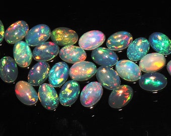 May include: A collection of oval-shaped opals with iridescent colors, including green, blue, red, and yellow. The opals are arranged in a curved line on a black background.