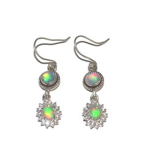 Peut inclure: Une paire de boucles d'oreilles pendantes en argent. Chaque boucle d'oreille présente une pierre d'opale ronde sertie dans un cadre en métal torsadé, avec une opale plus petite en dessous, entourée d'un halo de pierres précieuses rondes et claires. Les opales affichent un jeu de couleurs.