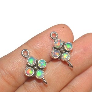 May include: Two silver-toned opal charms, each featuring four iridescent opal stones. The opals display a range of colors, including green, yellow, and red. The charms have a small loop at the top for attachment, and a decorative silver base.