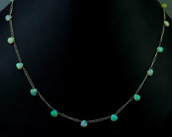 May include: A silver chain necklace with teardrop-shaped opal stones. The necklace is on a black background.