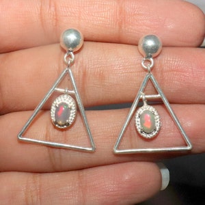 May include: A pair of silver triangle earrings with a small oval opal gemstone hanging from each triangle.