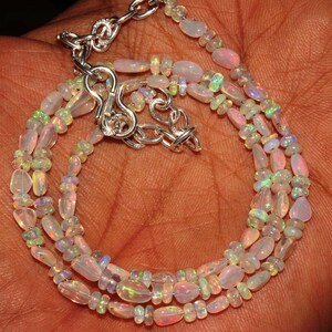 May include: A multi-strand necklace made of white opal beads with a silver clasp. The necklace is made of three strands of oval-shaped beads.