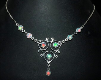 May include: A silver necklace with a delicate, intricate design featuring a pendant with multiple iridescent opal stones. The necklace has a chain with small opal stones.