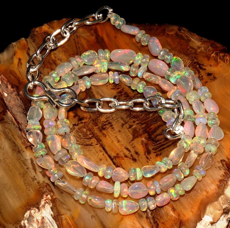May include: A multi-strand necklace made of iridescent opal beads in various shapes and sizes. The necklace is secured with a silver clasp and chain.