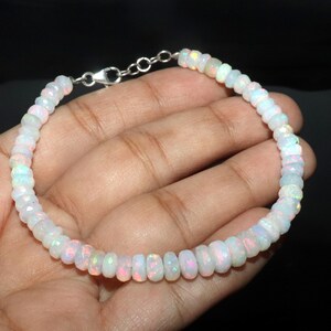 May include: A white opal bead bracelet with a silver clasp. The beads have a subtle iridescence, with hints of pink, blue, and green. The bracelet is strung on a delicate chain.