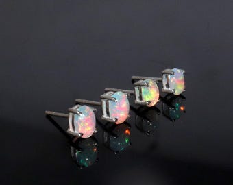 May include: Four silver stud earrings with oval-shaped opal gemstones. The opals have a white base with iridescent rainbow colors.