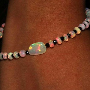 May include: A delicate bracelet made with white opal beads and black onyx beads. A larger white opal stone is the centerpiece of the bracelet.