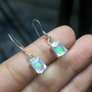 Peut inclure: Boucles d'oreilles pendantes en argent avec des pierres d'opale rectangulaires. Les opales présentent un jeu de couleurs vives, avec des éclats de vert, de bleu et de jaune. Design simple et élégant.
