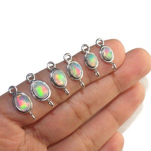 May include: Six oval opal pendants with silver settings. Each pendant has a loop at the top and a small hook at the bottom. The opals show a vibrant play of colour, including green, pink, and yellow hues.