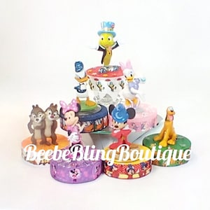 Puede incluir: Un conjunto de seis figuras de personajes de Disney de colores sobre pequeñas bases redondas. Las figuras incluyen Mickey Mouse, Minnie Mouse, Donald Duck, Goofy, Pluto y Chip y Dale. Las bases están decoradas con motivos de Disney.