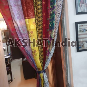 May include: A colorful curtain made of repurposed fabric panels. The curtain is tied together with a brown cord. The curtain is hanging in a doorway.