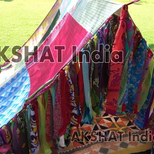 May include: A colourful fabric play tent with a patchwork design and a fringe of fabric strips hanging from the bottom. The tent is set up on a green grassy lawn. The text "AKSHAT India" is visible on the tent.