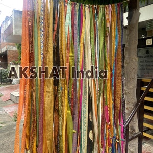 May include: A colorful fabric curtain made of many strips of fabric in various colors, patterns, and textures. The curtain is hanging from a string and is being used as a backdrop for a photo shoot. The text "AKSHAT India" is visible in the center of the image.