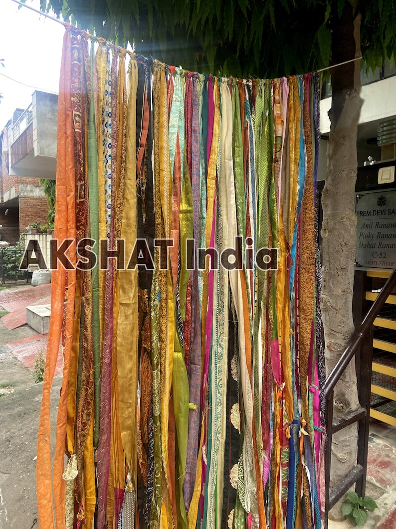 May include: A colorful fabric curtain made of many strips of fabric in various colors, patterns, and textures. The curtain is hanging from a string and is being used as a backdrop for a photo shoot. The text "AKSHAT India" is visible in the center of the image.