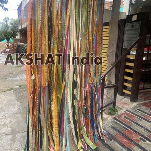 May include: A colorful curtain made of many strips of fabric, hanging in front of a brick wall. The fabric is in various shades of green, yellow, orange, pink, blue, and purple. The curtain is about 9 feet tall and 6 feet wide.