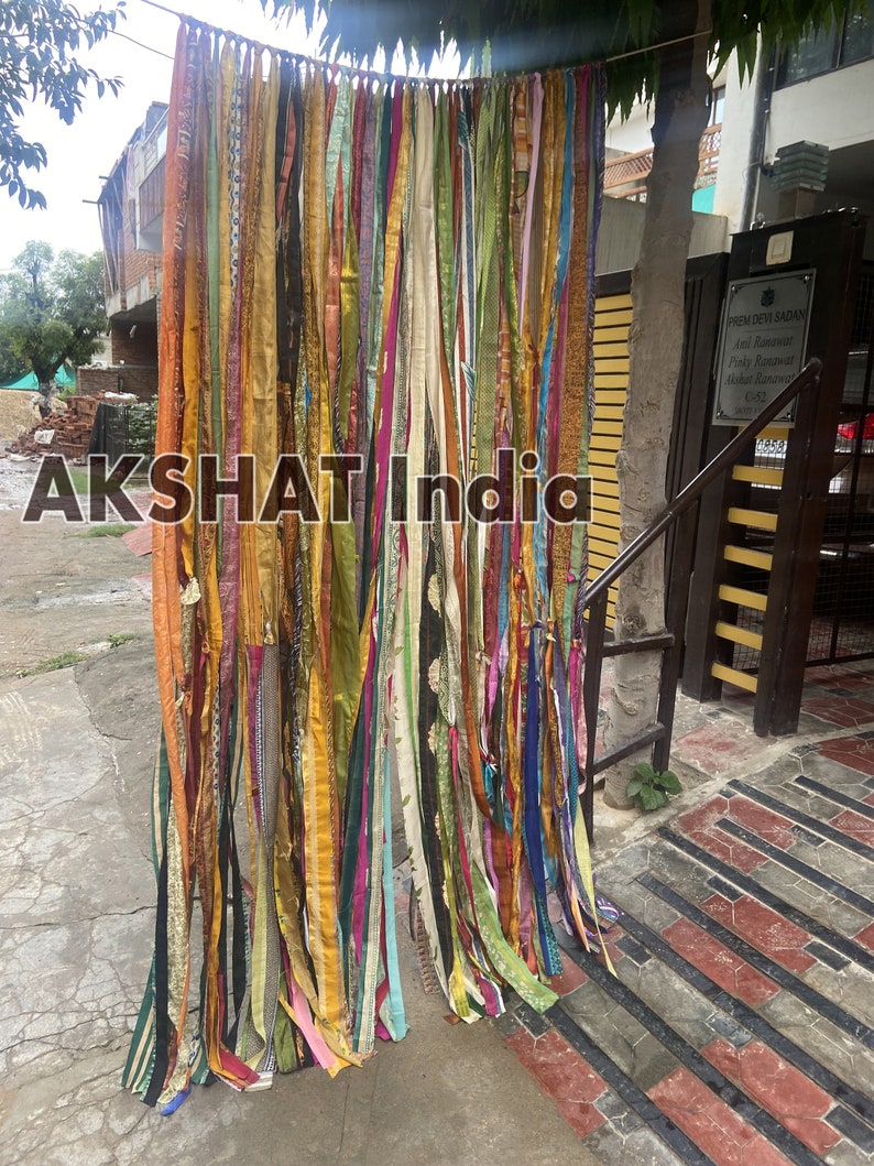 May include: A colorful curtain made of many strips of fabric, hanging in front of a brick wall. The fabric is in various shades of green, yellow, orange, pink, blue, and purple. The curtain is about 9 feet tall and 6 feet wide.