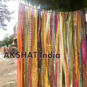 May include: A colorful fabric curtain made of many strips of fabric in various colors and patterns, including orange, yellow, green, blue, and purple. The fabric is tied together at the top and hangs down in a cascade of color. The text "AKSHAT India" is visible at the bottom of the image.