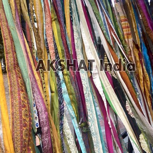 May include: A wall decorated with colorful fabric strips hanging from the top. The strips are of various lengths and widths, and they are arranged in a random pattern. The fabric is a mix of different colors, patterns, and textures. The text "AKSHAT India" is visible in the center of the image.