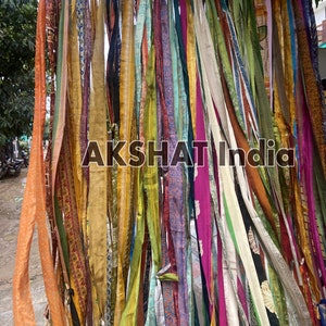 May include: A colorful curtain made of many strips of fabric in various colors, including orange, yellow, green, blue, purple, and pink. The fabric strips are tied together at the top and hang down in a cascade. The text "AKSHAT India" is visible in the center of the image.