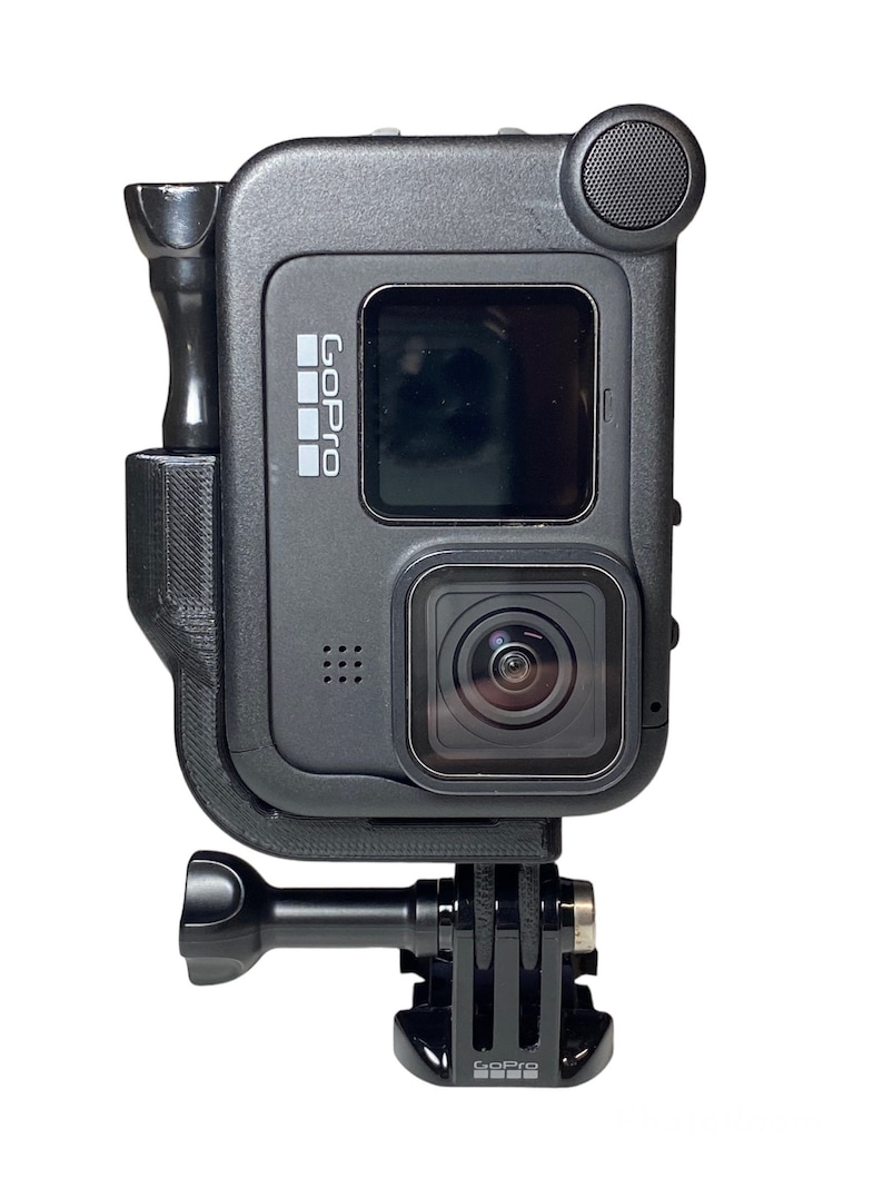 May include: Black GoPro action camera with a black protective case and a GoPro logo on the side. The camera has a small screen on the back and a lens on the front. The camera is attached to a black GoPro mount.