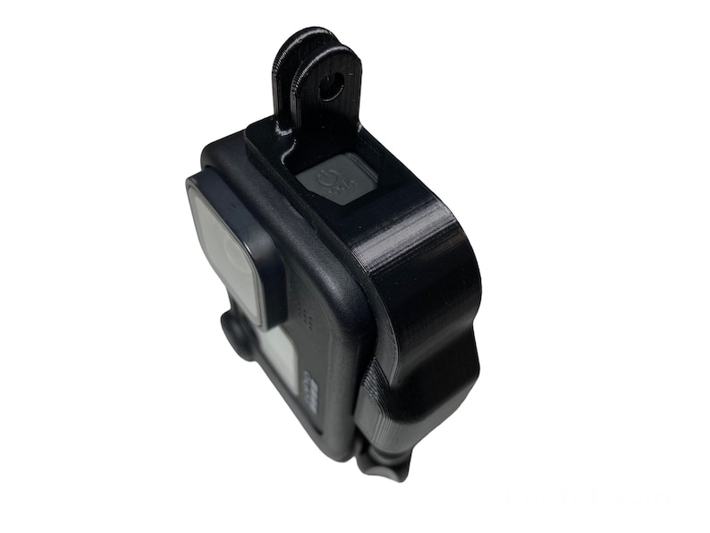 May include: Black GoPro camera with a black protective case and a black mount on top. The camera has a small screen on the back and a lens on the front.