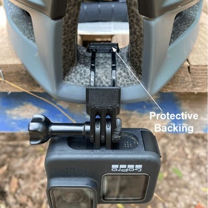 Puede incluir: Una c&aacute;mara GoPro negra montada en un casco mediante un soporte de pl&aacute;stico negro con respaldo protector. La c&aacute;mara est&aacute; orientada hacia adelante.