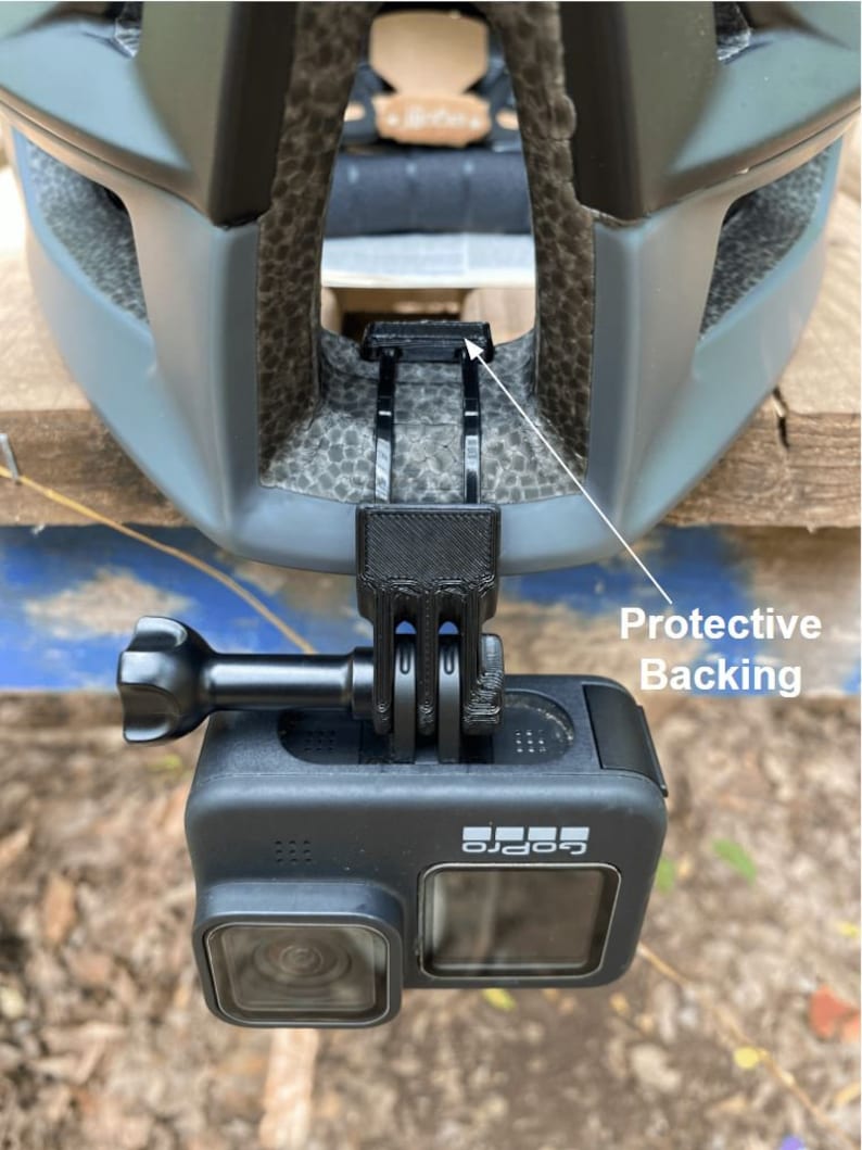 Puede incluir: Una c&aacute;mara GoPro negra montada en un casco mediante un soporte de pl&aacute;stico negro con respaldo protector. La c&aacute;mara est&aacute; orientada hacia adelante.