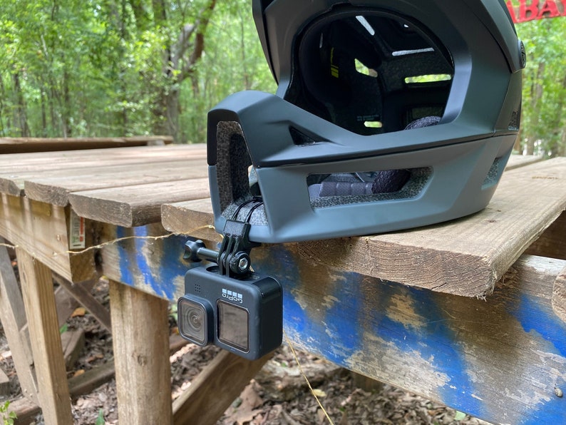 Puede incluir: Una c&aacute;mara GoPro negra con dos lentes montada en un casco usando un soporte GoPro negro.