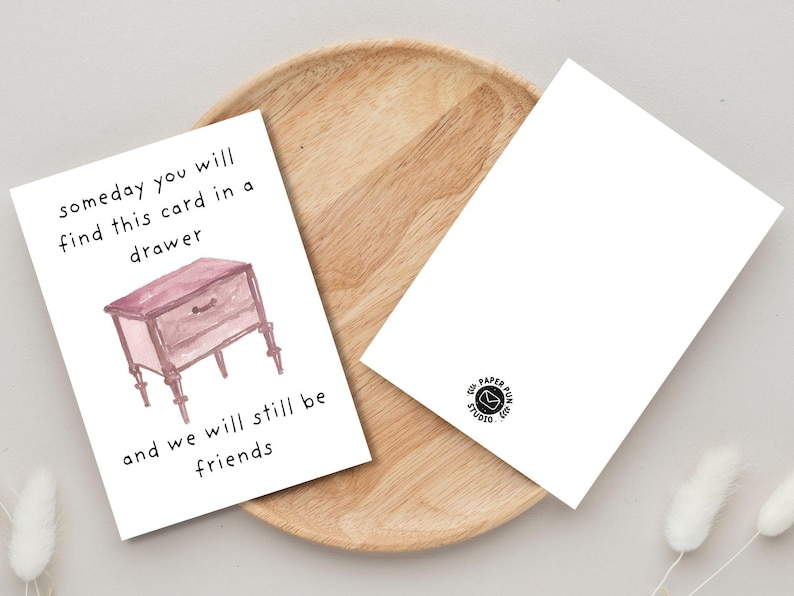 Peut inclure: Deux cartes de v&oelig;ux blanches sur un plateau en bois. L'une d'elles pr&eacute;sente une illustration &agrave; l'aquarelle d'une petite commode et le texte "someday you will find this card in a drawer and we will still be friends."