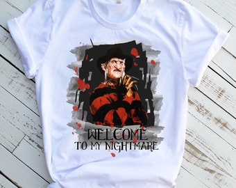 May include: White t-shirt with a graphic print of Freddy Krueger from the movie "A Nightmare on Elm Street". The graphic is in black, red, and gray with a watercolor effect. The text "Welcome to my nightmare" is printed below the graphic.