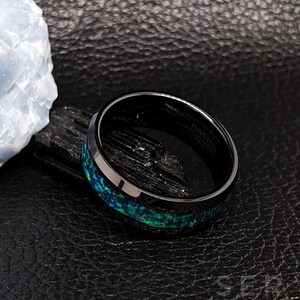 May include: Black tungsten carbide ring with a green and blue opal inlay. The ring is engraved with the words "Tungsten Carbide".