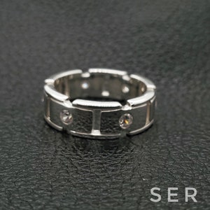 May include: A silver band ring with a textured surface and small clear stones set into the band.