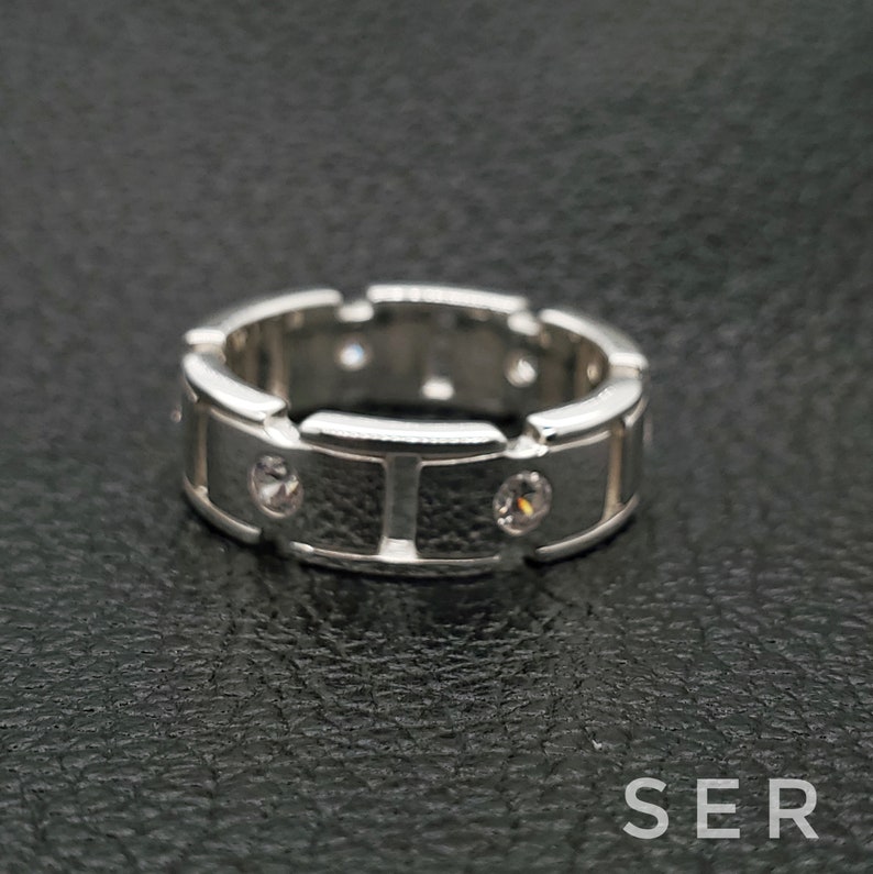 May include: A silver band ring with a textured surface and small clear stones set into the band.