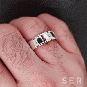 May include: A silver ring with a rectangular design and three small clear stones.
