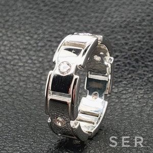 May include: A silver ring with a unique design featuring multiple small clear stones. The ring has a textured, almost chain-like design.