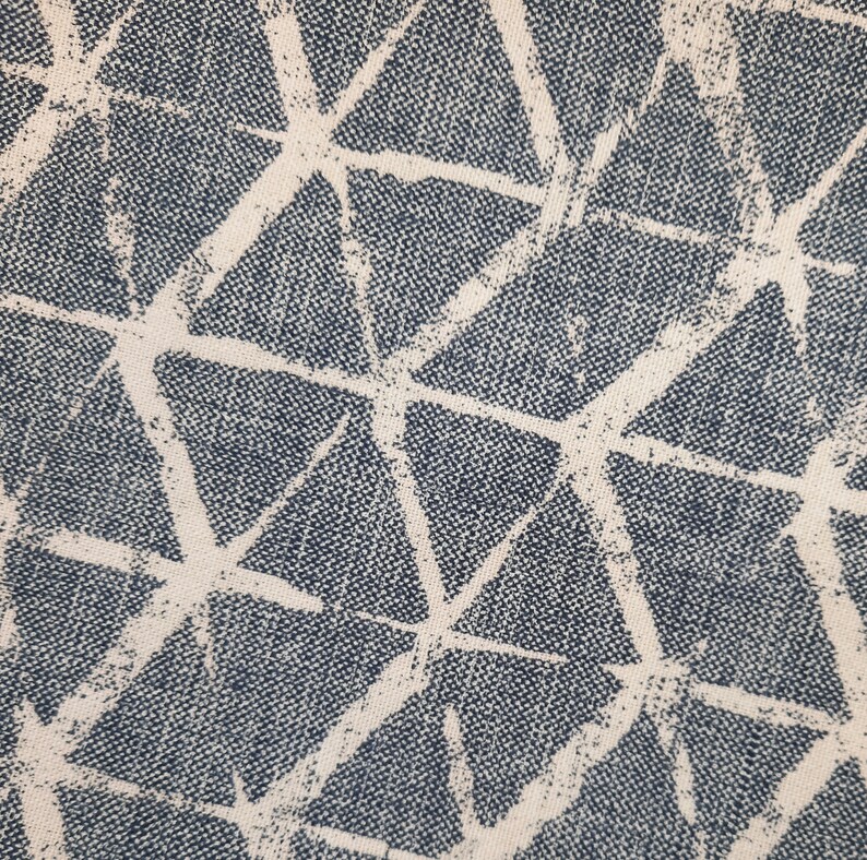 Puede incluir: Primer plano de una tela con un patr&oacute;n geom&eacute;trico de tri&aacute;ngulos blancos sobre un fondo azul oscuro.