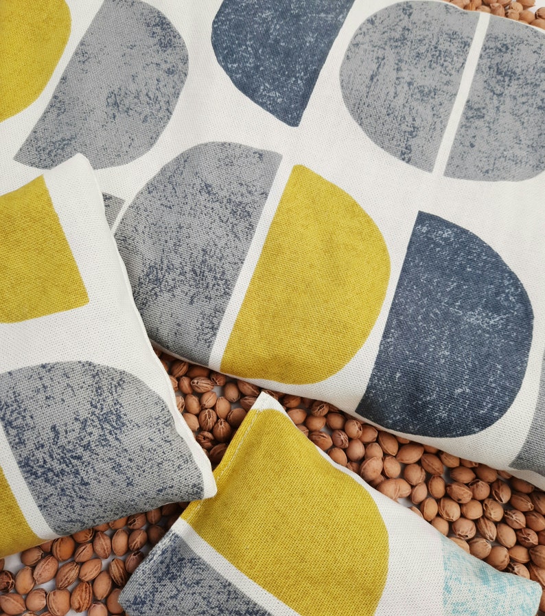 Puede incluir: Dos almohadas con un patr&oacute;n geom&eacute;trico de semic&iacute;rculos amarillos y grises. Las almohadas est&aacute;n sobre una superficie cubierta de nueces marrones.