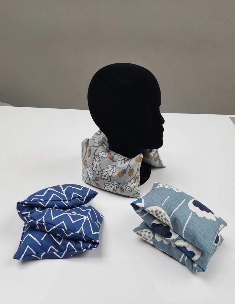 Puede incluir: Tres almohadas de cuello de tela, una con un patr&oacute;n de chevron azul y blanco, otra con un patr&oacute;n floral azul y blanco y otra con un patr&oacute;n de bellota gris y blanco.